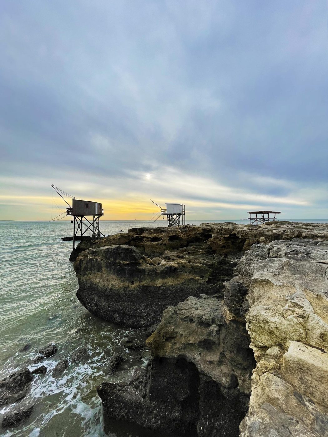 Trois carrelets sur pilotis alignés sur le platier rocheux au crépuscule, face à l'océan Atlantique